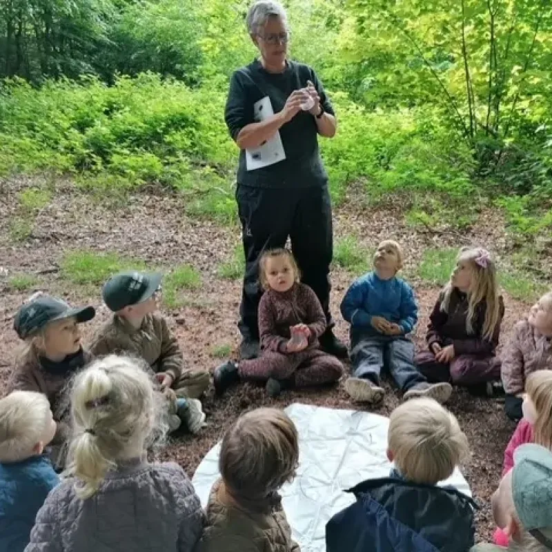 Pædagog der står og snakker til en cirkel af børn ude i Hadsten skov